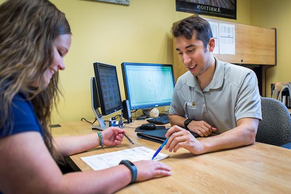 Two individuals looking at a sheet of paper, with one pointing at the paper.